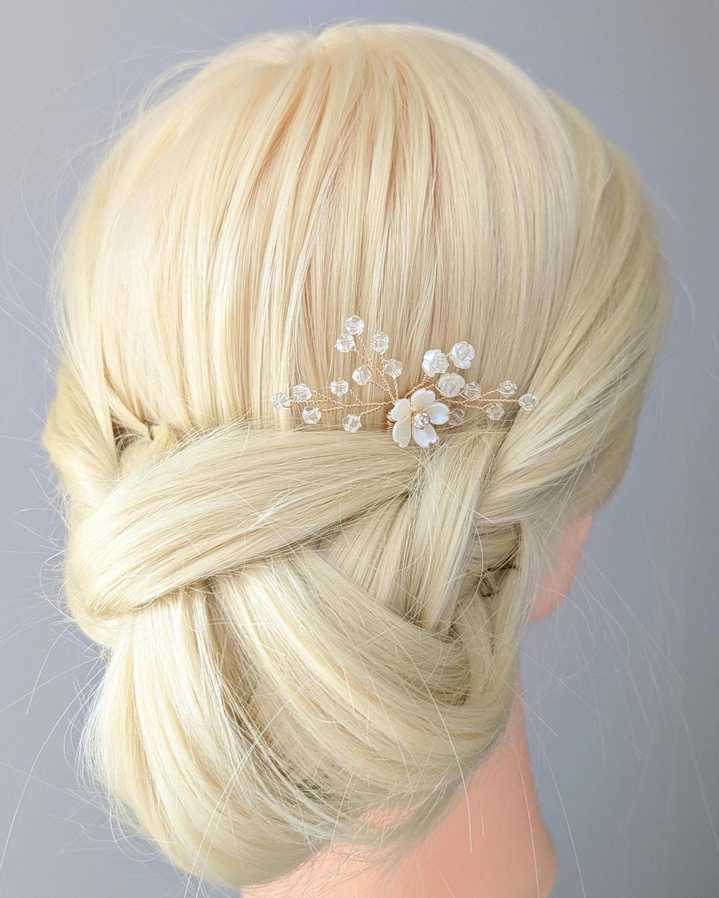 Blonde hair styled in an intricate braid with decorative pins against a gray background