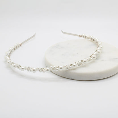 A delicate headband with a thin silver wire adorned with small white pearls of various sizes. The pearls are evenly spaced along the curved band. The minimalist, open-ended design provides an elegant and adjustable fit.