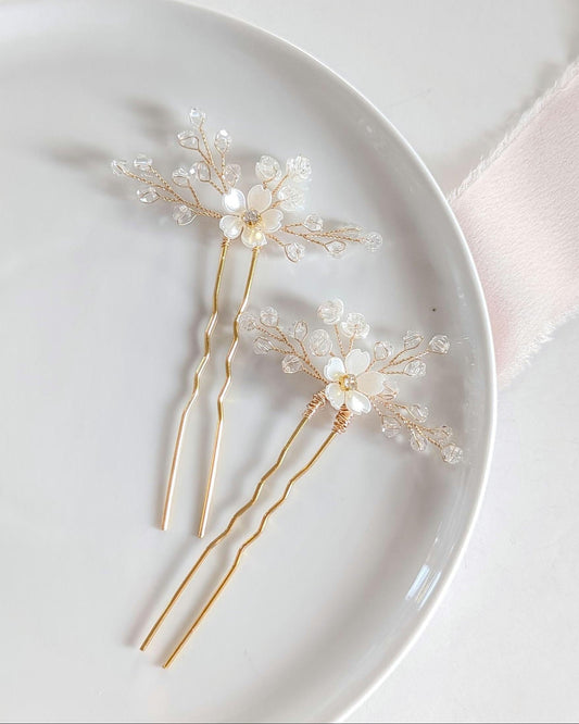 Two decorative hairpins with floral and crystal designs on a white plate.