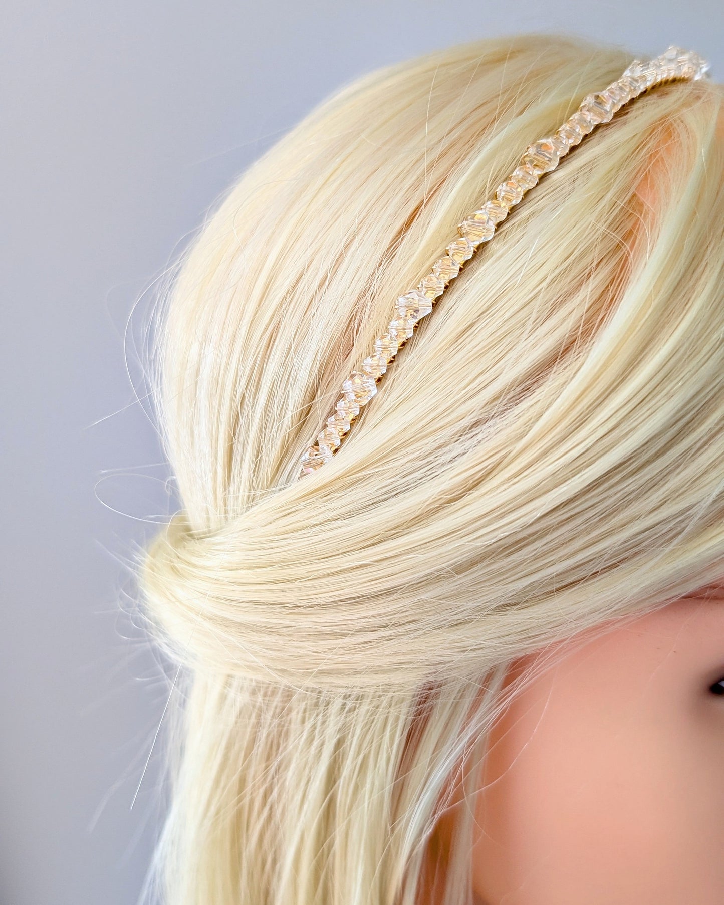 Close-up of a person with blonde hair wearing a thin clear crystal headband against a light gray background