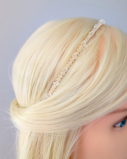 A close up of a head with blonde hair wearing a decorative headband against a gray background