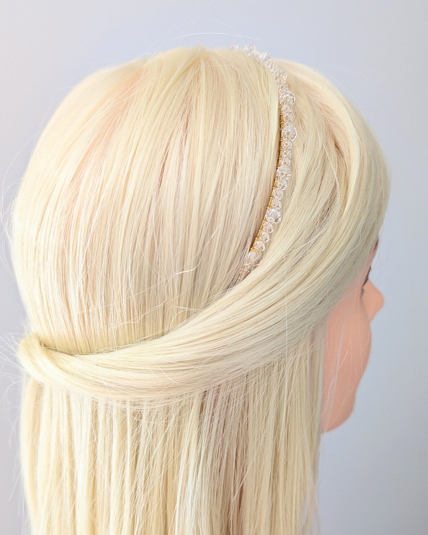 Mannequin head with blonde hair and a decorative headband on a light gray background