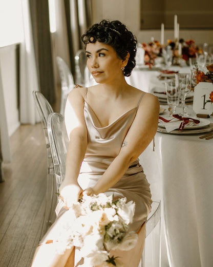 Woman in a beige dress holding a bouquet at a decorated table with a thin crystal headband styled in her hair