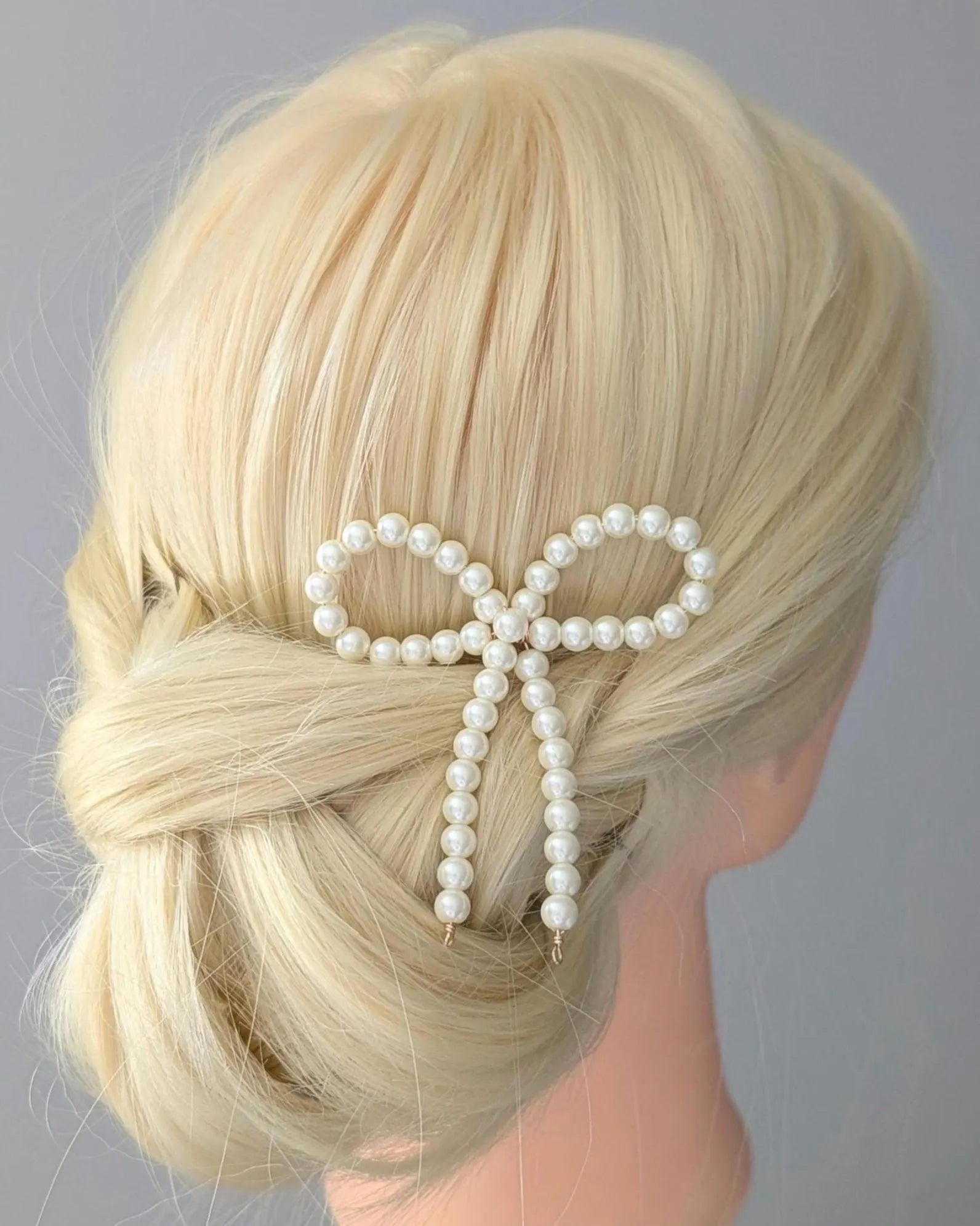 Blonde hair styled with a pearl bow accessory on a gray background