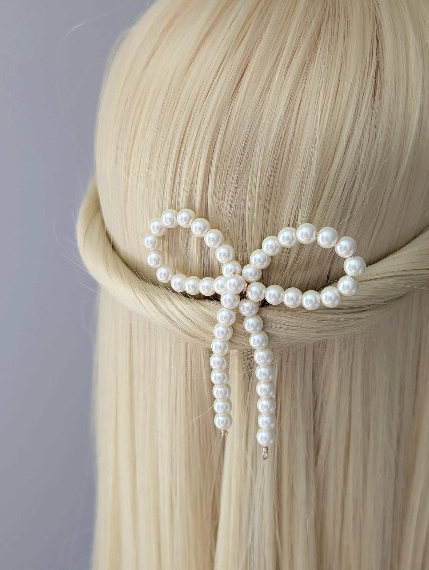 Pearl hair clip in the shape of a bow on blonde hair against a gray background