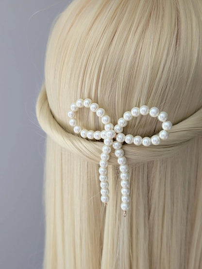 Pearl hair clip in the shape of a bow on blonde hair against a gray background