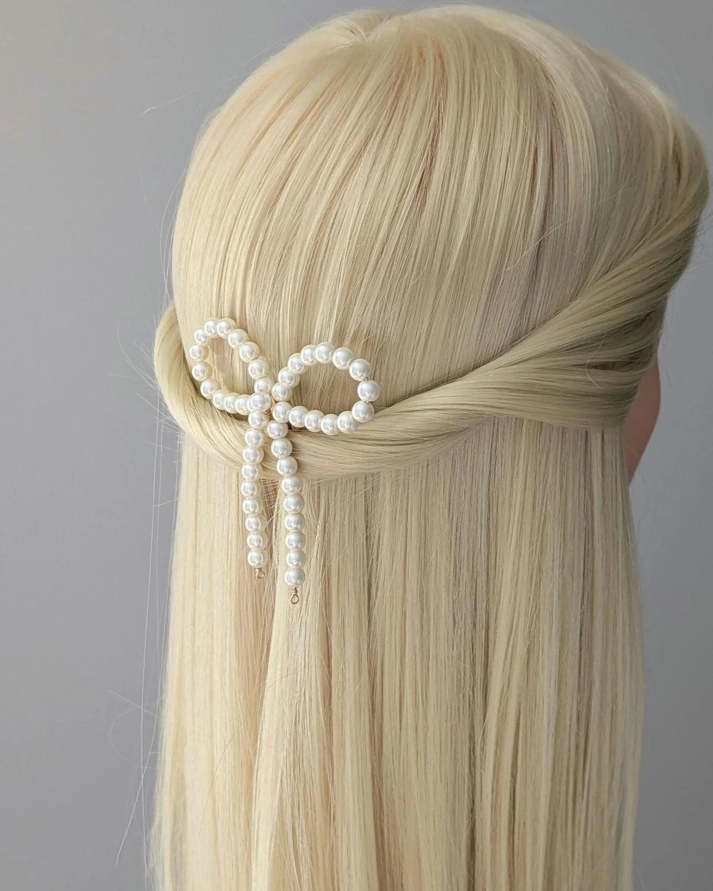 Blonde hair styled with a decorative bow made of pearls against a gray background