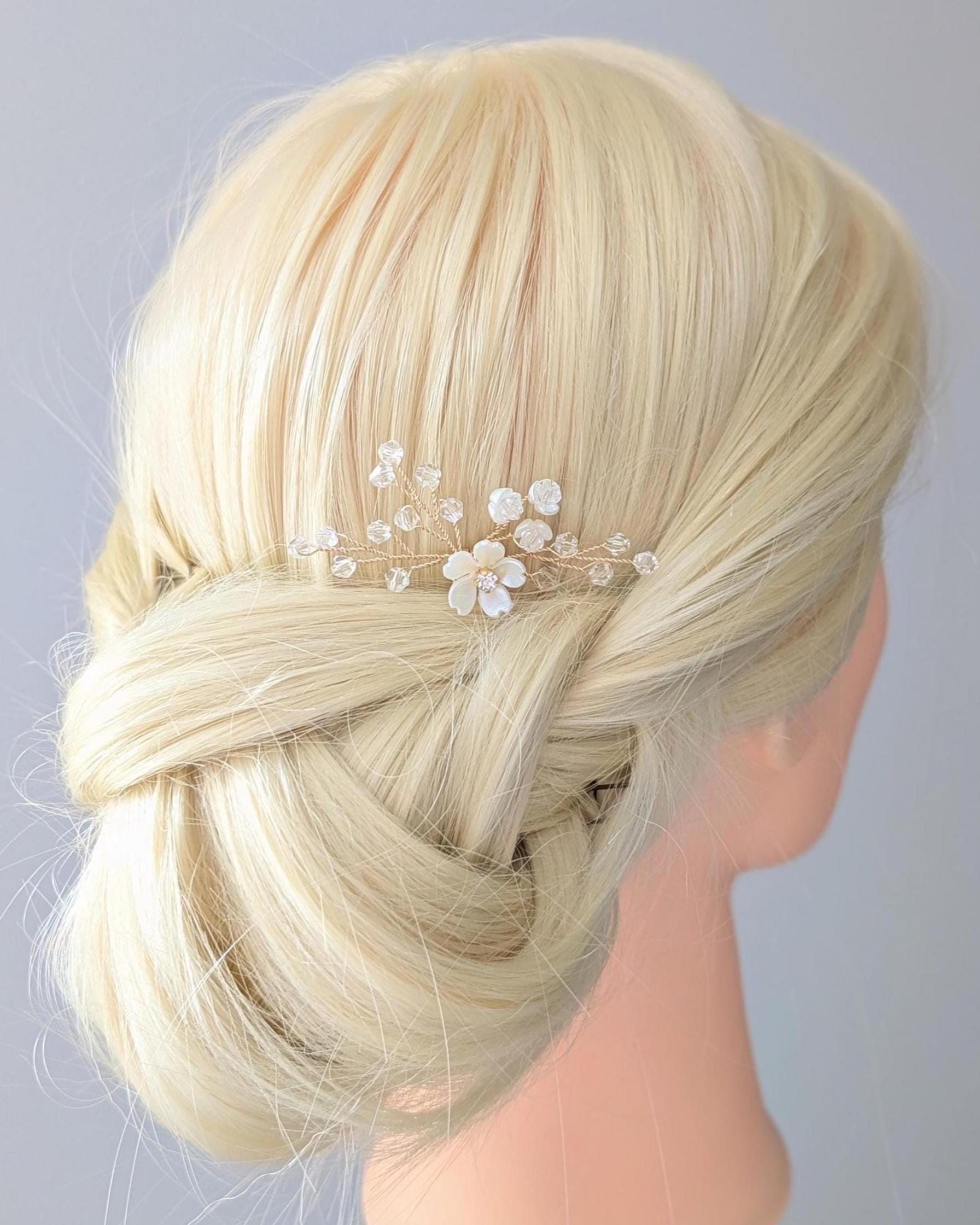 Blonde hair styled in an updo with a decorative floral hairpin on a mannequin head against a light gray background