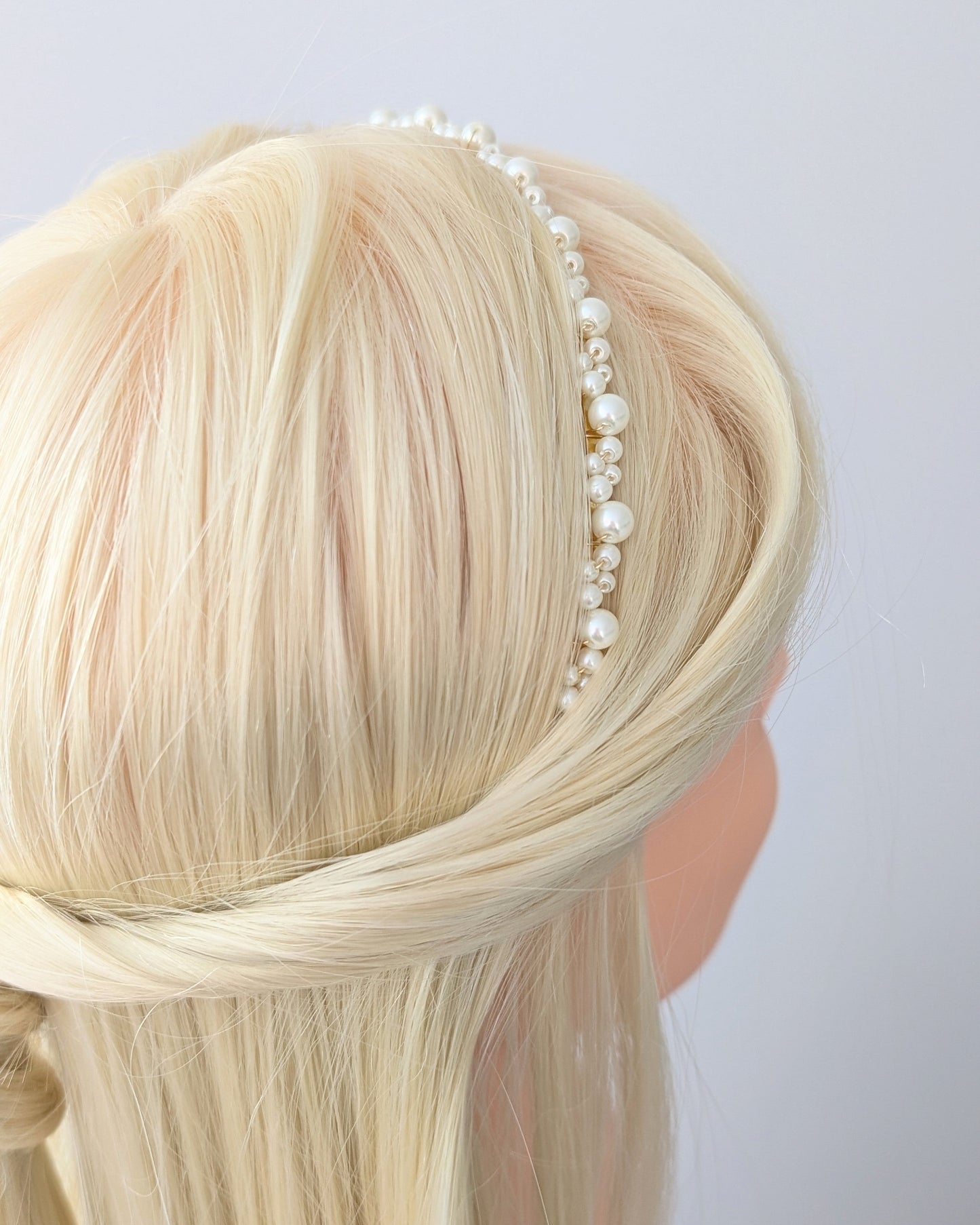 Blonde hair with a pearl headband on a plain background